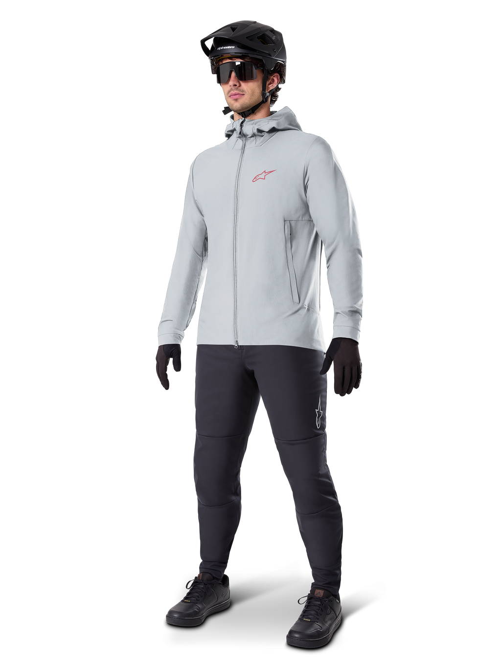 Chaqueta térmica Alpinestars A-Dura en Titanium, chaqueta de ciclismo con capucha en gris claro con logotipo rojo de Alpinestars en el pecho, usada por un hombre con casco de MTB negro, gafas de sol, pantalones gris oscuro y guantes negros, equipamiento profesional de mountain bike