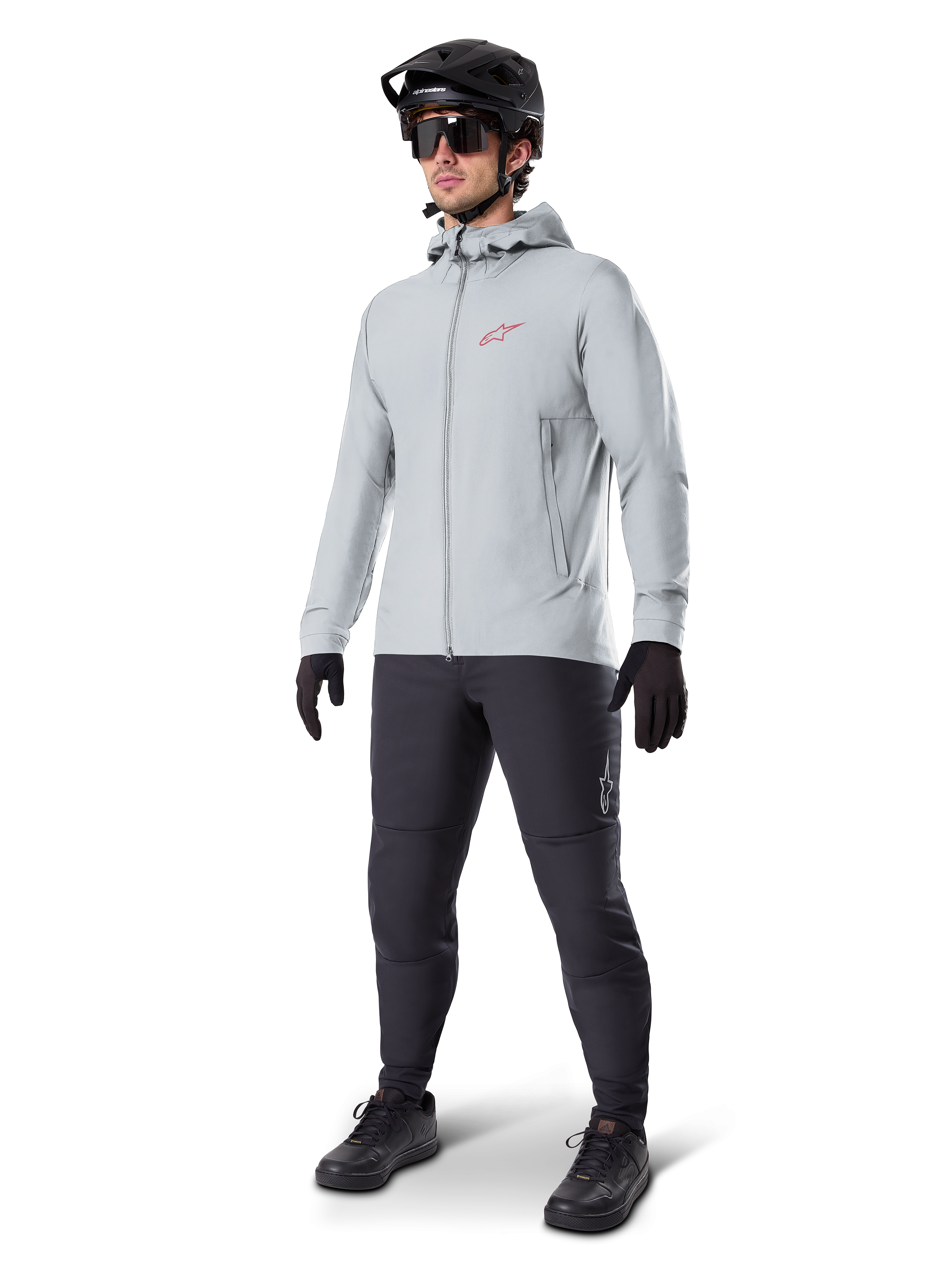Chaqueta térmica Alpinestars A-Dura en Titanium, chaqueta de ciclismo con capucha en gris claro con logotipo rojo de Alpinestars en el pecho, usada por un hombre con casco de MTB negro, gafas de sol, pantalones gris oscuro y guantes negros, equipamiento profesional de mountain bike