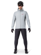 Chaqueta térmica Alpinestars A-Dura, gris titanio, chaqueta de ciclismo usada con pantalones de ciclismo de montaña negros, guantes y casco, con un pequeño logotipo de estrella roja en el pecho y cremallera frontal completa, equipo aislante ligero para ciclismo todoterreno.