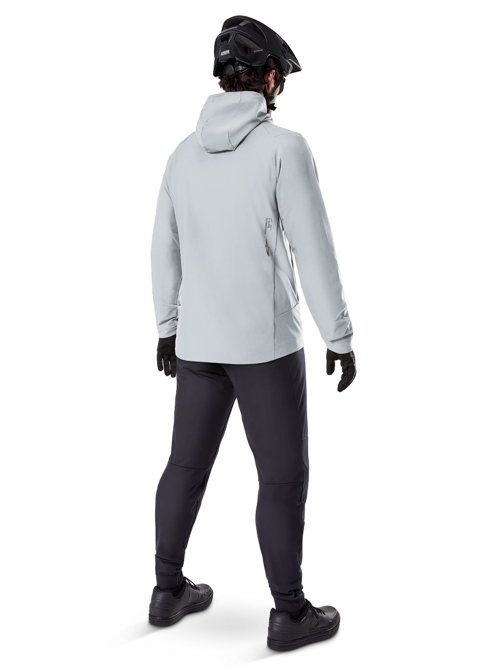 Alpinestars A-Dura Thermal Jacket en Titanium, vista trasera de ciclista masculino vistiendo chaqueta térmica gris claro con capucha, combinada con casco de MTB negro, guantes negros y pantalones gris oscuro, equipo funcional para ciclismo de montaña.