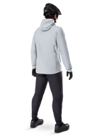 Alpinestars A-Dura Thermal Jacket en Titanium, vista trasera de ciclista masculino vistiendo chaqueta térmica gris claro con capucha, combinada con casco de MTB negro, guantes negros y pantalones gris oscuro, equipo funcional para ciclismo de montaña.