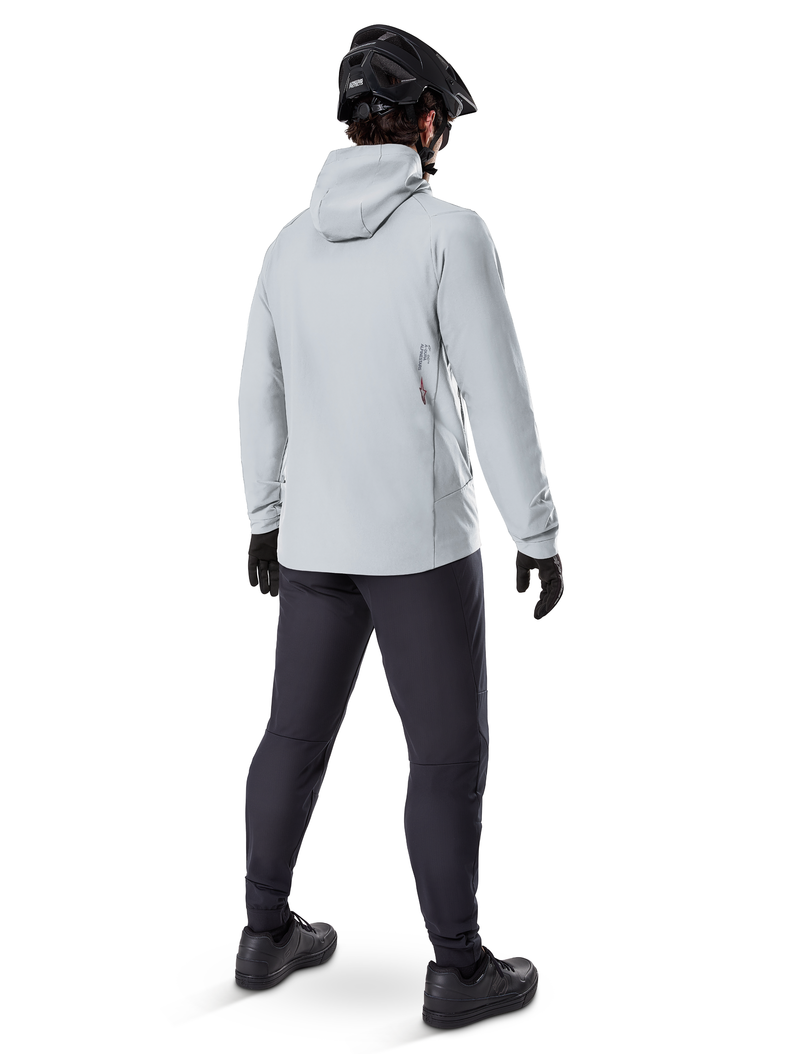 Alpinestars A-Dura Thermal Jacket en Titanium, vista trasera de ciclista masculino vistiendo chaqueta térmica gris claro con capucha, combinada con casco de MTB negro, guantes negros y pantalones gris oscuro, equipo funcional para ciclismo de montaña.
