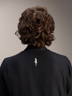 Chaqueta cortavientos Alpinestars A-Aria, negra, primer plano de la parte posterior de los hombros y el cuello, con un pequeño logotipo blanco en el centro de la espalda, usada por un modelo con cabello castaño ondulado, equipamiento de ciclismo de rendimiento minimalista