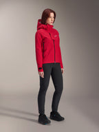 Chaqueta impermeable Alpinestars Stella A-Dura Elite para mujer, rojo flúor, chaqueta con capucha para ciclismo de montaña con el logotipo blanco de Astars en la solapa del pecho, combinada con pantalones negros y zapatillas de montaña negras, equipamiento técnico de alto rendimiento para trail