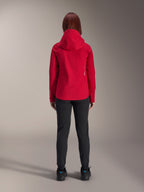 Vista posterior de una mujer con la chaqueta impermeable Alpinestars Stella A-Dura Elite en Rojo Fluo, combinada con pantalones y calzado negros, con capucha protectora y dobladillo trasero más largo para ciclismo de montaña