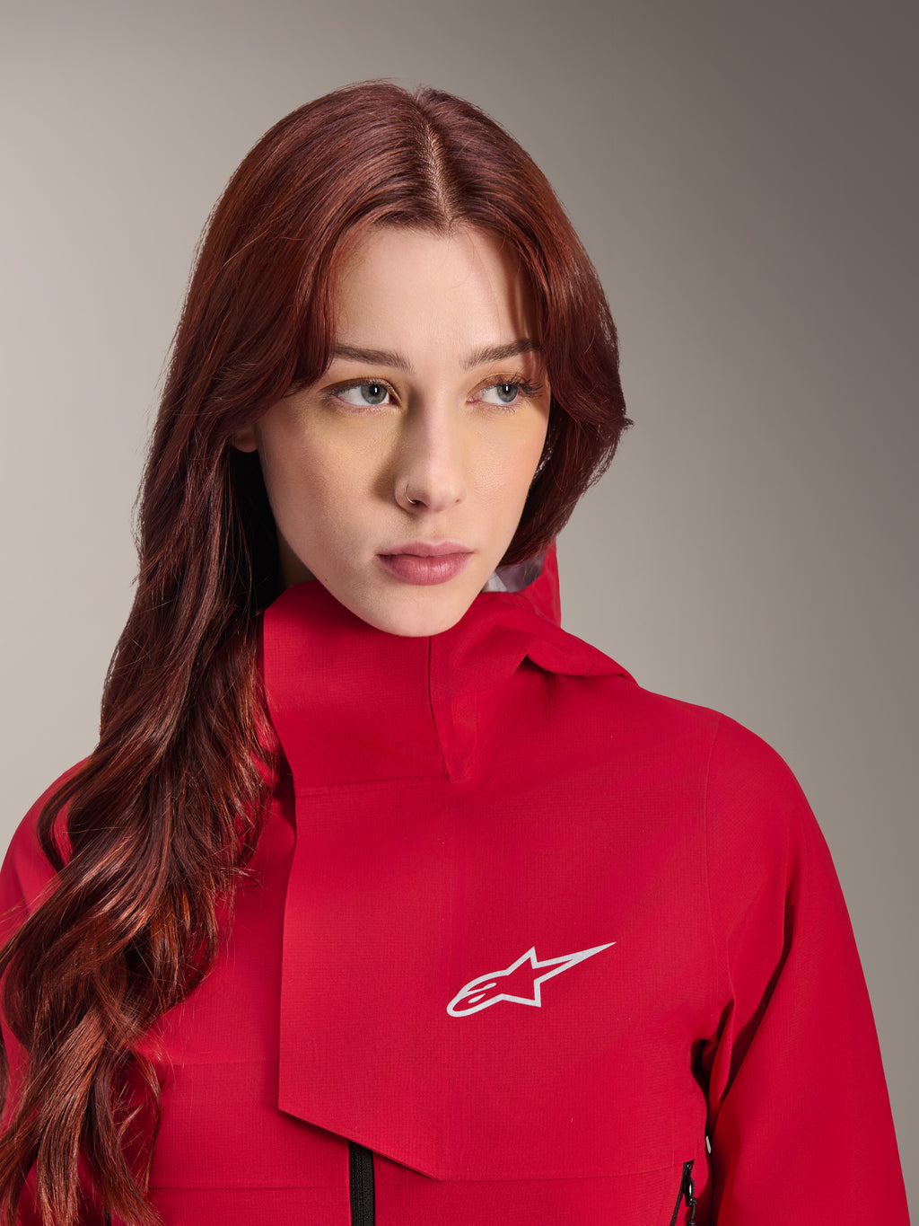 Chaqueta impermeable Alpinestars Stella A-Dura Elite, Rojo Fluo, usada por una mujer con cabello largo y pelirrojo, chaqueta técnica impermeable de 3 capas con cuello alto y logotipo blanco, equipamiento de alto rendimiento para exteriores y ciclismo de montaña