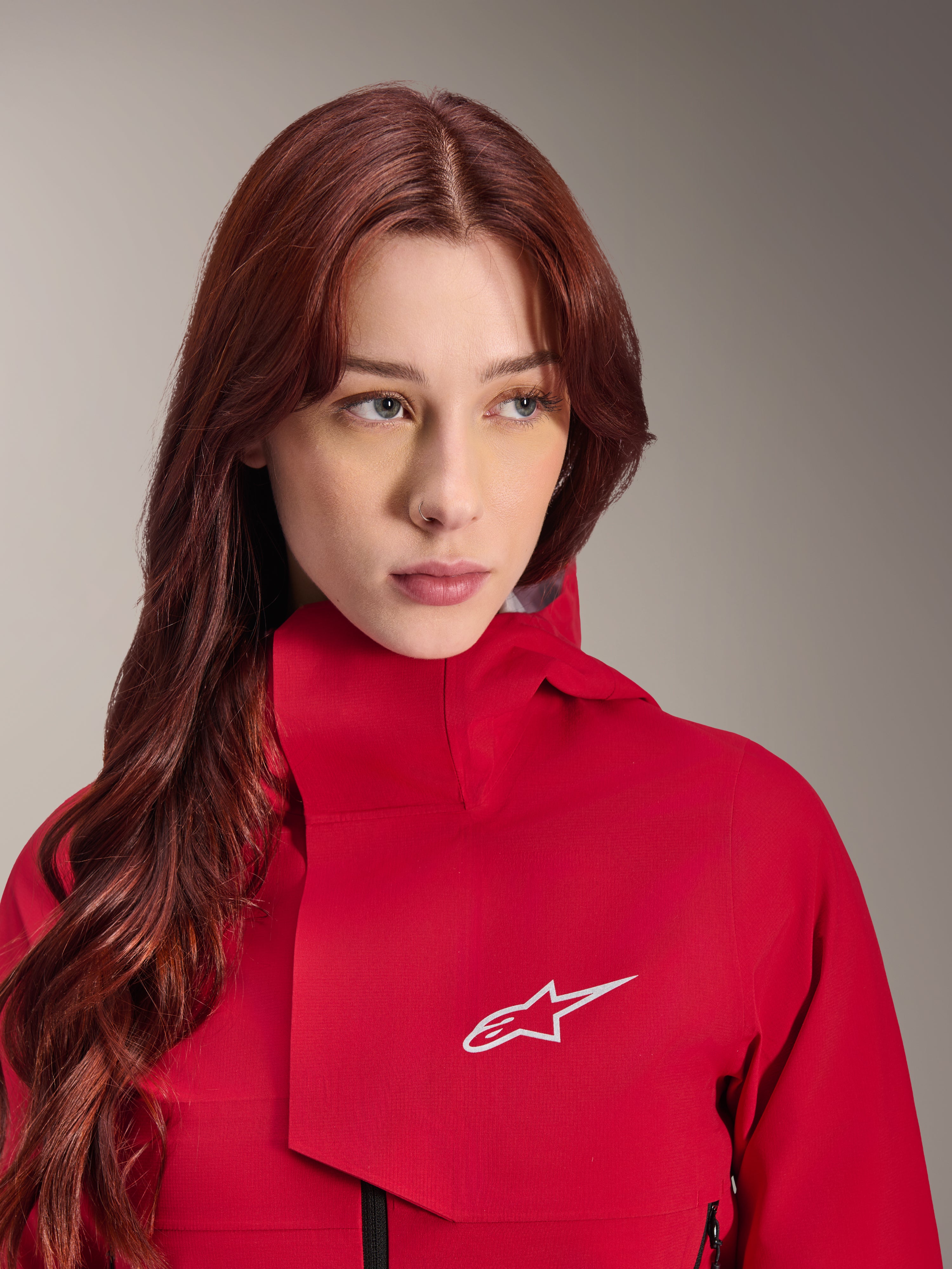 Chaqueta impermeable Alpinestars Stella A-Dura Elite, Rojo Fluo, usada por una mujer con cabello largo y pelirrojo, chaqueta técnica impermeable de 3 capas con cuello alto y logotipo blanco, equipamiento de alto rendimiento para exteriores y ciclismo de montaña