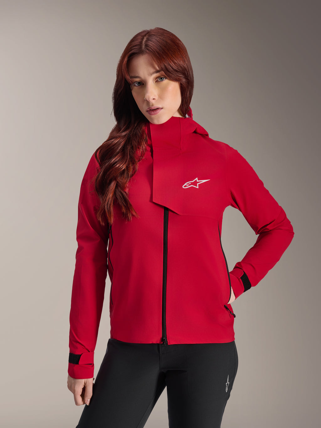 Chaqueta impermeable Alpinestars Stella A-Dura Elite, chaqueta de ciclismo de montaña para mujer, rojo flúor, con solapa frontal con el logotipo blanco de Alpinestars, cuello alto y puños ajustables, combinada con pantalones negros para un estilo de conducción técnico