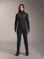 Mujer con chaqueta térmica Alpinestars Stella A-Dura, negra, chaqueta de ciclismo con aislamiento ligero y capucha, logo blanco de Astars en el pecho, combinada con pantalones negros y zapatillas deportivas