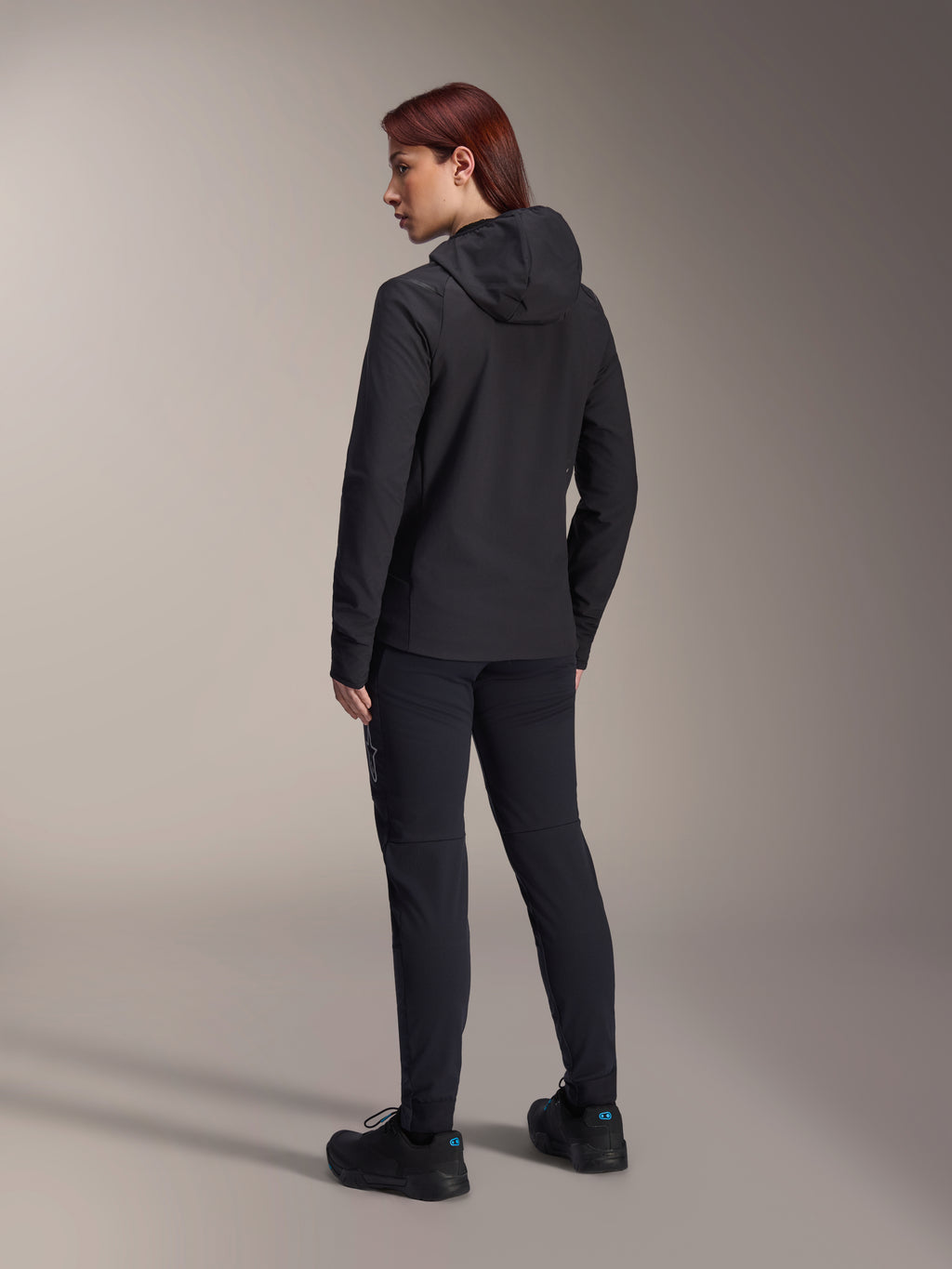 Chaqueta térmica Alpinestars Stella A-Dura, chaqueta de ciclismo MTB para mujer, negra, vista posterior que destaca la capucha aislante y el ajuste regular, combinada con pantalones y calzado negros a juego, aislamiento térmico ligero para rodar en climas fríos