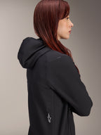 Chaqueta térmica Alpinestars Stella A-Dura, chaqueta de ciclismo para mujer, color negro, perfil lateral de una mujer con cabello pelirrojo luciendo la chaqueta, cuenta con capucha integrada y logotipo de la estrella de Alpinestars en blanco en el lateral, equipo térmico ligero y aislado para MTB