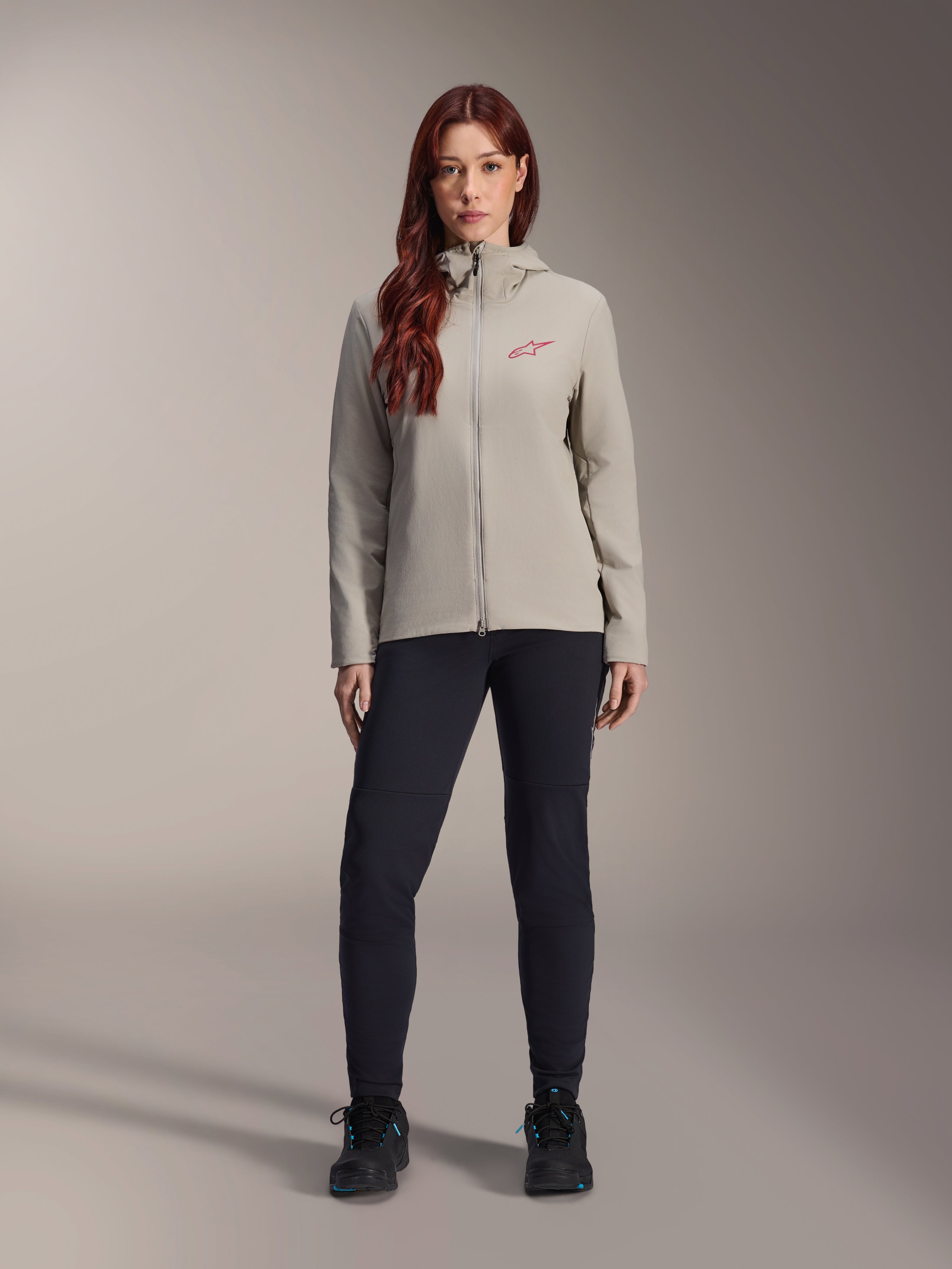 Alpinestars Stella A-Dura Thermal Jacket para mujer, chaqueta de ciclismo de montaña, gris titanio, usada con pantalones técnicos negros y calzado negro, con capucha forrada de vellón y logotipo rojo en el pecho, diseñada para montar en climas fríos
