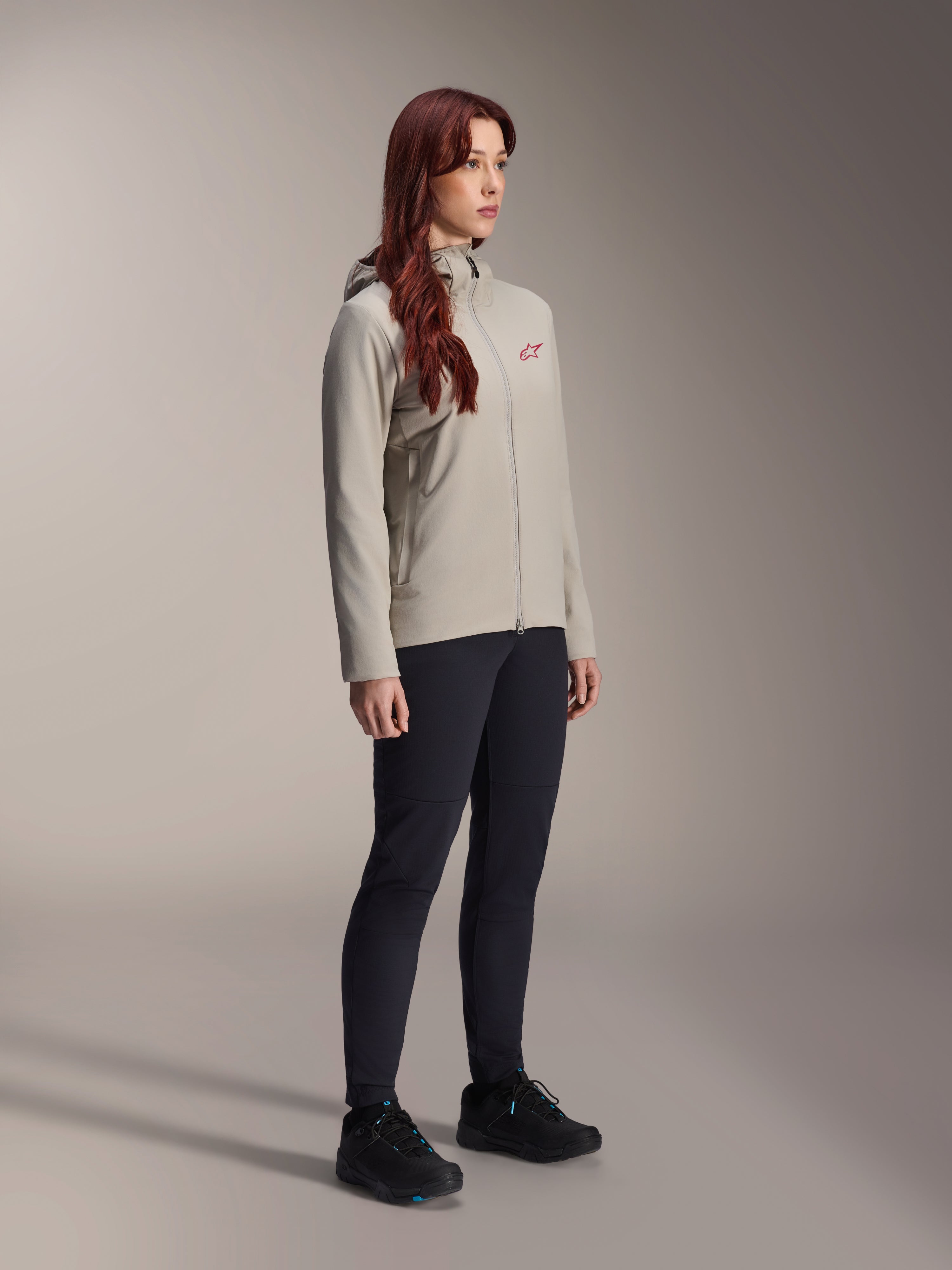 Chaqueta térmica Alpinestars Stella A-Dura, gris titanio, chaqueta térmica de ciclismo para mujer con un logotipo de estrella roja en el pecho, combinada con pantalones técnicos negros y zapatillas de ciclismo de montaña negras, fotografía de estudio de ropa para ciclismo