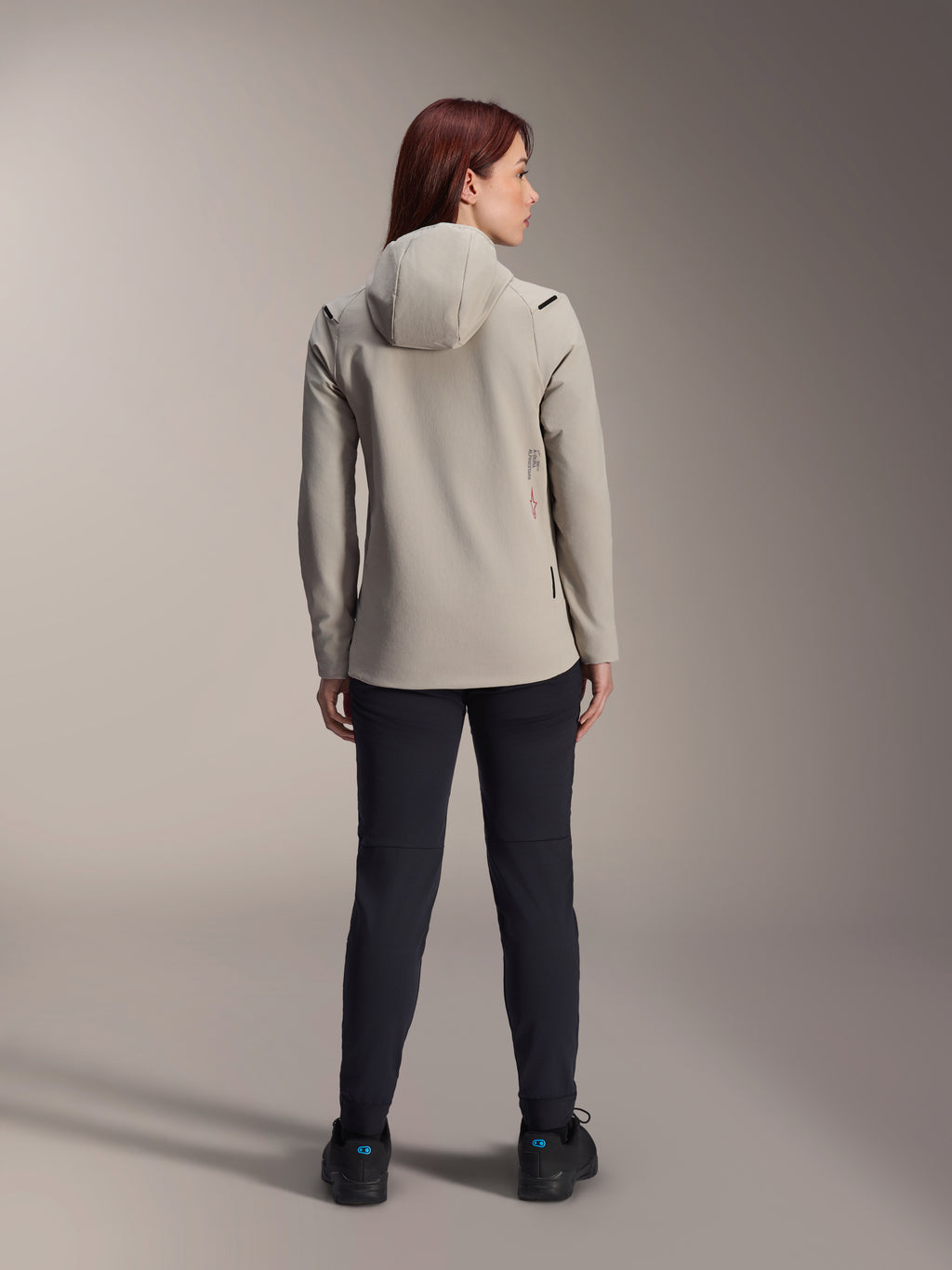 Chaqueta térmica Alpinestars Stella A-Dura para mujer, gris titanium, vista posterior con pantalones negros, con capucha aislante forrada de vellón y un pequeño logotipo rojo, chaqueta de ciclismo de montaña funcional y elegante para climas fríos.