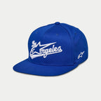 Gorra Alpinestars Los Angeles, gorra snapback de visera plana, azul con bordado 3D de 'Los Angeles' en blanco con fuente atlética, logotipo Ageless en el lateral, corona estructurada, accesorio casual inspirado en el automovilismo