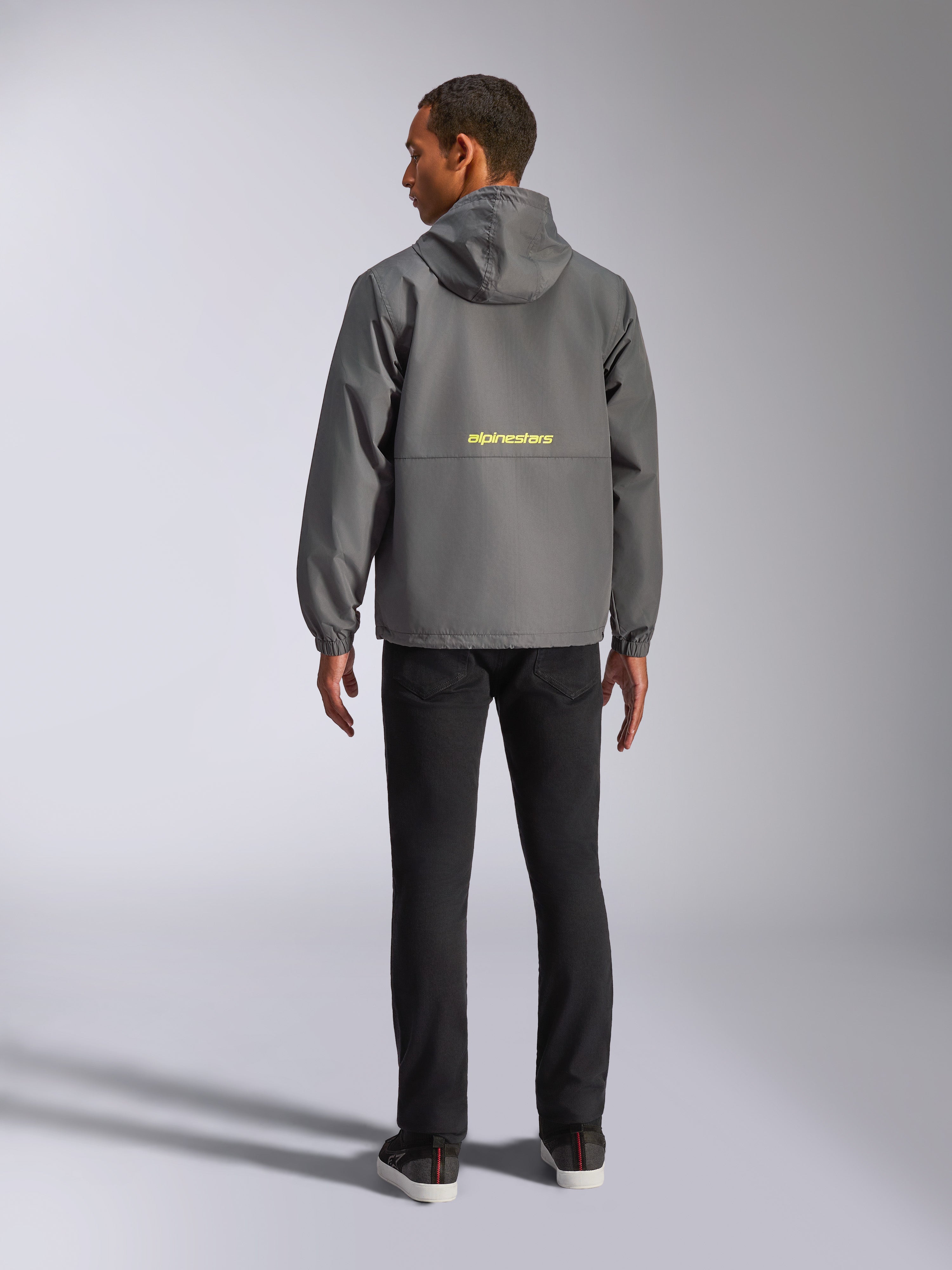 Chaqueta cortavientos Alpinestars Speeder Chromium, gris carbón y amarillo de alta visibilidad, vista trasera que muestra el logotipo amarillo de Alpinestars en el centro, cortavientos ligero con capucha y puños elásticos, ropa urbana de estilo casual inspirada en el automovilismo