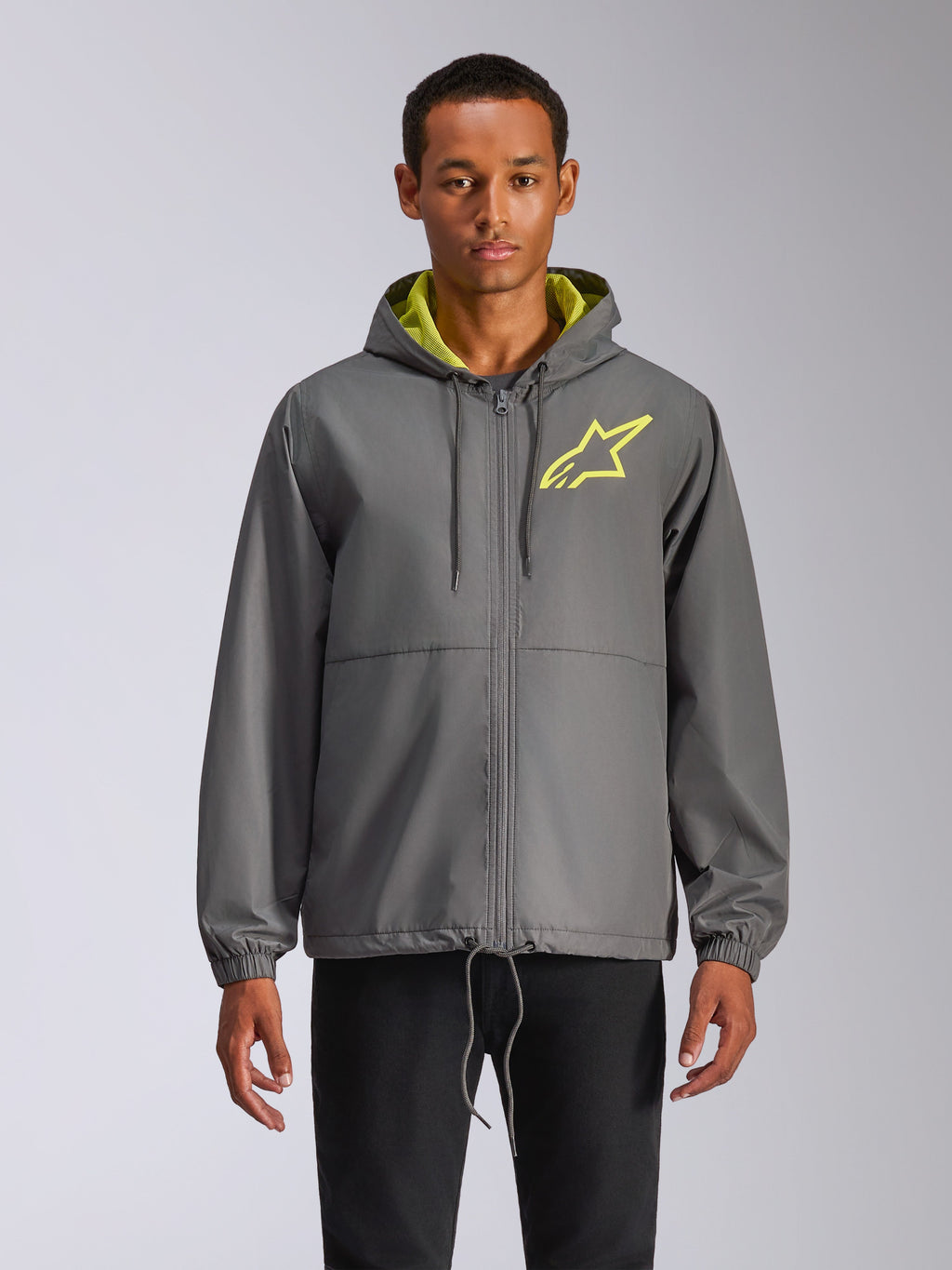 Chaqueta cortavientos Alpinestars Speeder Chromium, cortavientos gris carbón con capucha y logotipo de estrella en amarillo de alta visibilidad, interior de la capucha en verde lima, puños elásticos, cordones ajustables, cierre de cremallera frontal, estilo motorsport casual