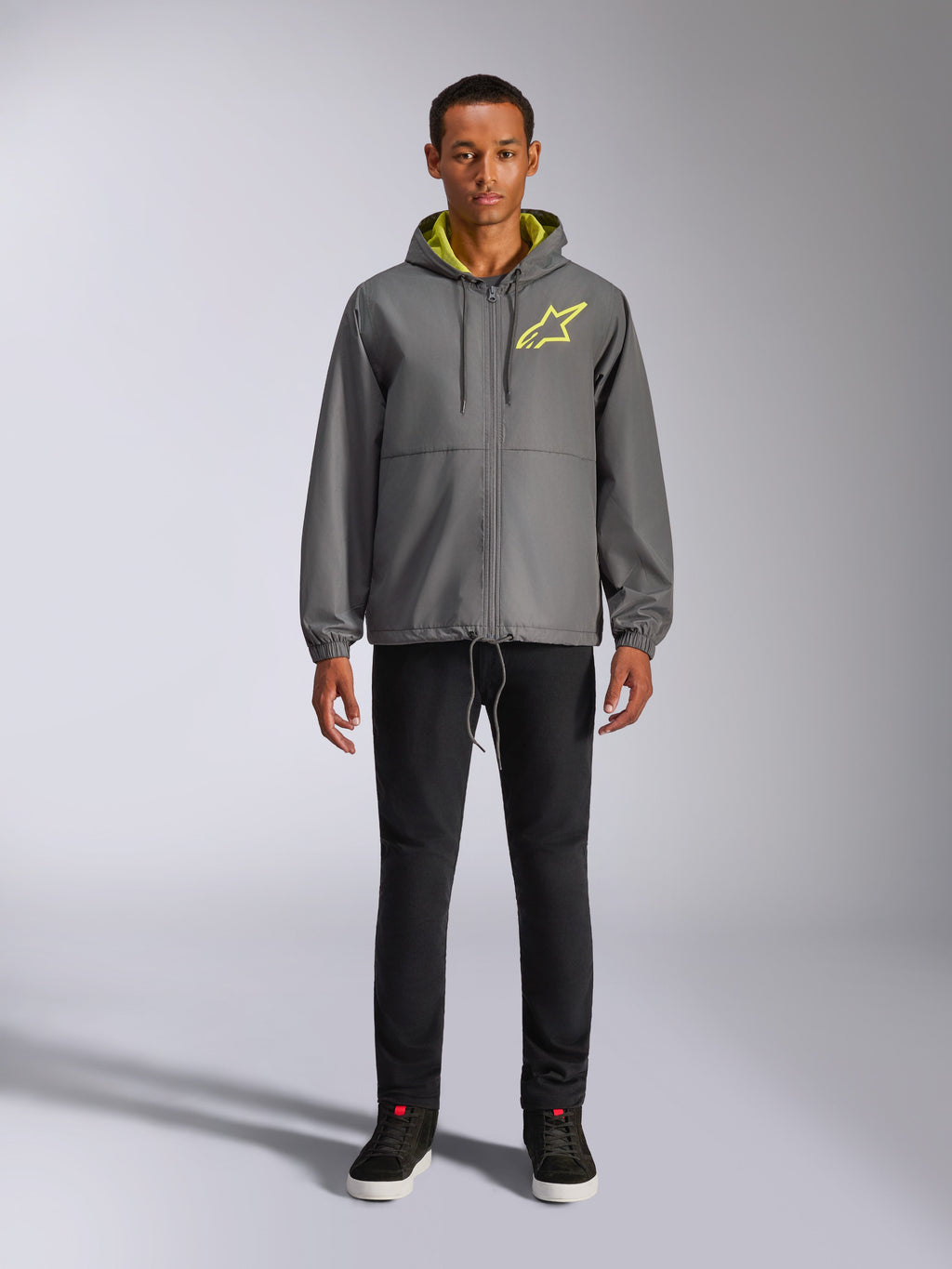 Alpinestars Speeder Chromium Windbreak Jacket, chaqueta con capucha gris carbón con forro y logotipo en el pecho en amarillo de alta visibilidad, cremallera frontal completa, puños elásticos, ropa urbana informal inspirada en el automovilismo