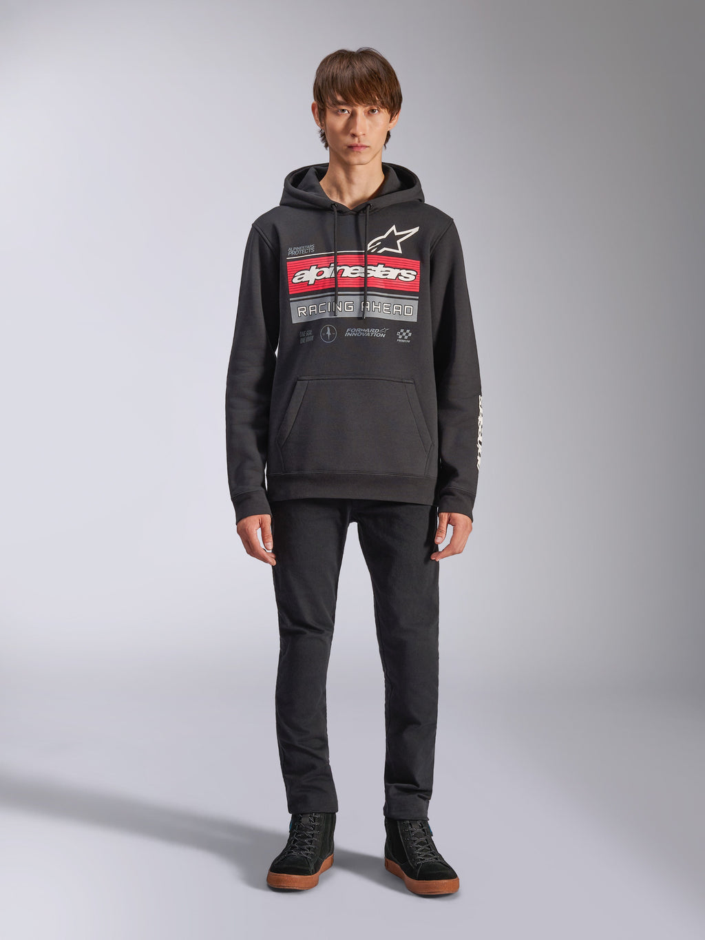 Alpinestars Harken Hoodie, sudadera negra con capucha, gráfico llamativo en el pecho con franjas rojas y el texto 'Racing Ahead', logotipo Astars blanco, bolsillo canguro, capucha con cordón, ropa urbana casual inspirada en el automovilismo