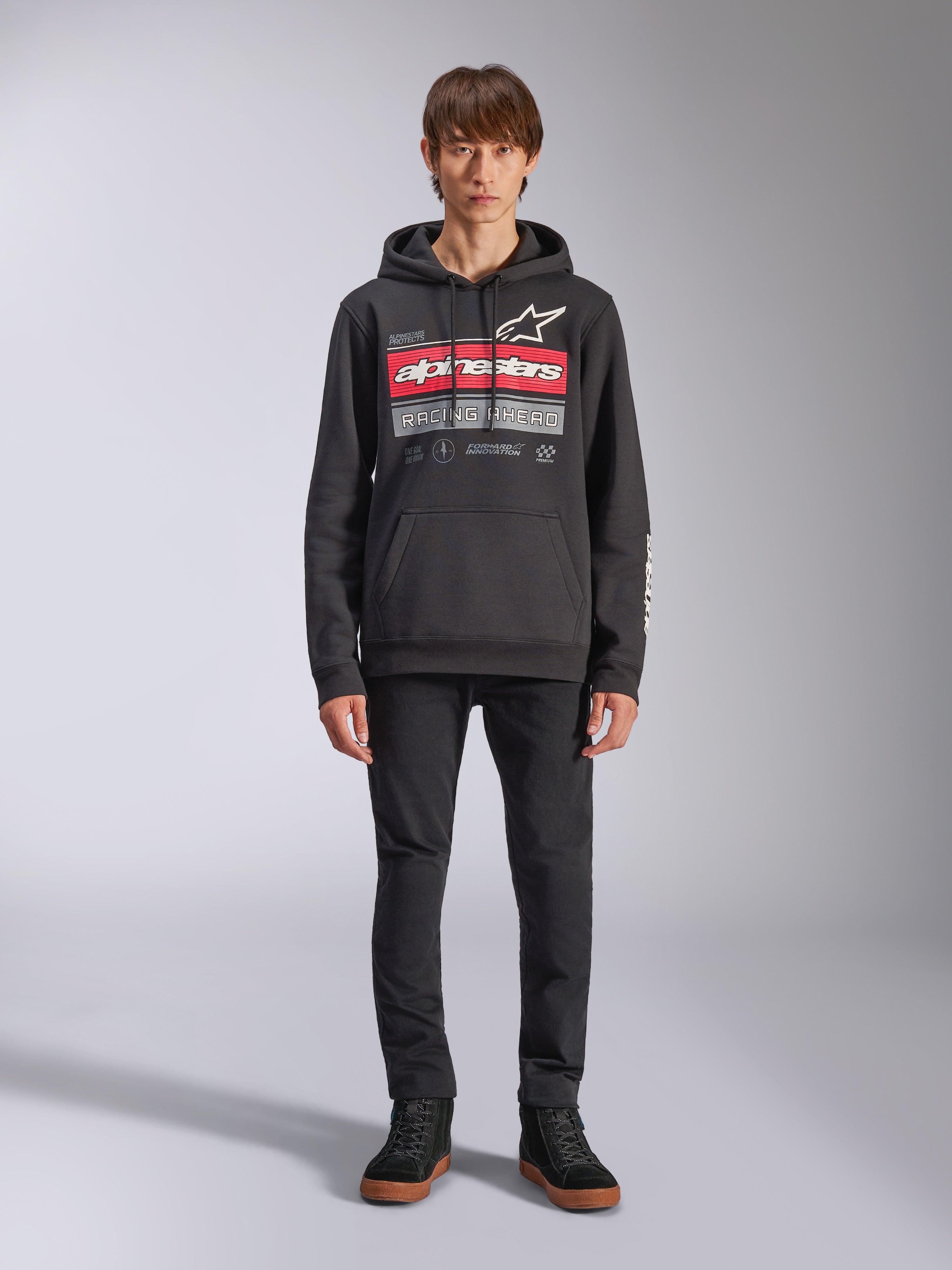 Alpinestars Harken Hoodie, sudadera negra con capucha, gráfico llamativo en el pecho con franjas rojas y el texto 'Racing Ahead', logotipo Astars blanco, bolsillo canguro, capucha con cordón, ropa urbana casual inspirada en el automovilismo