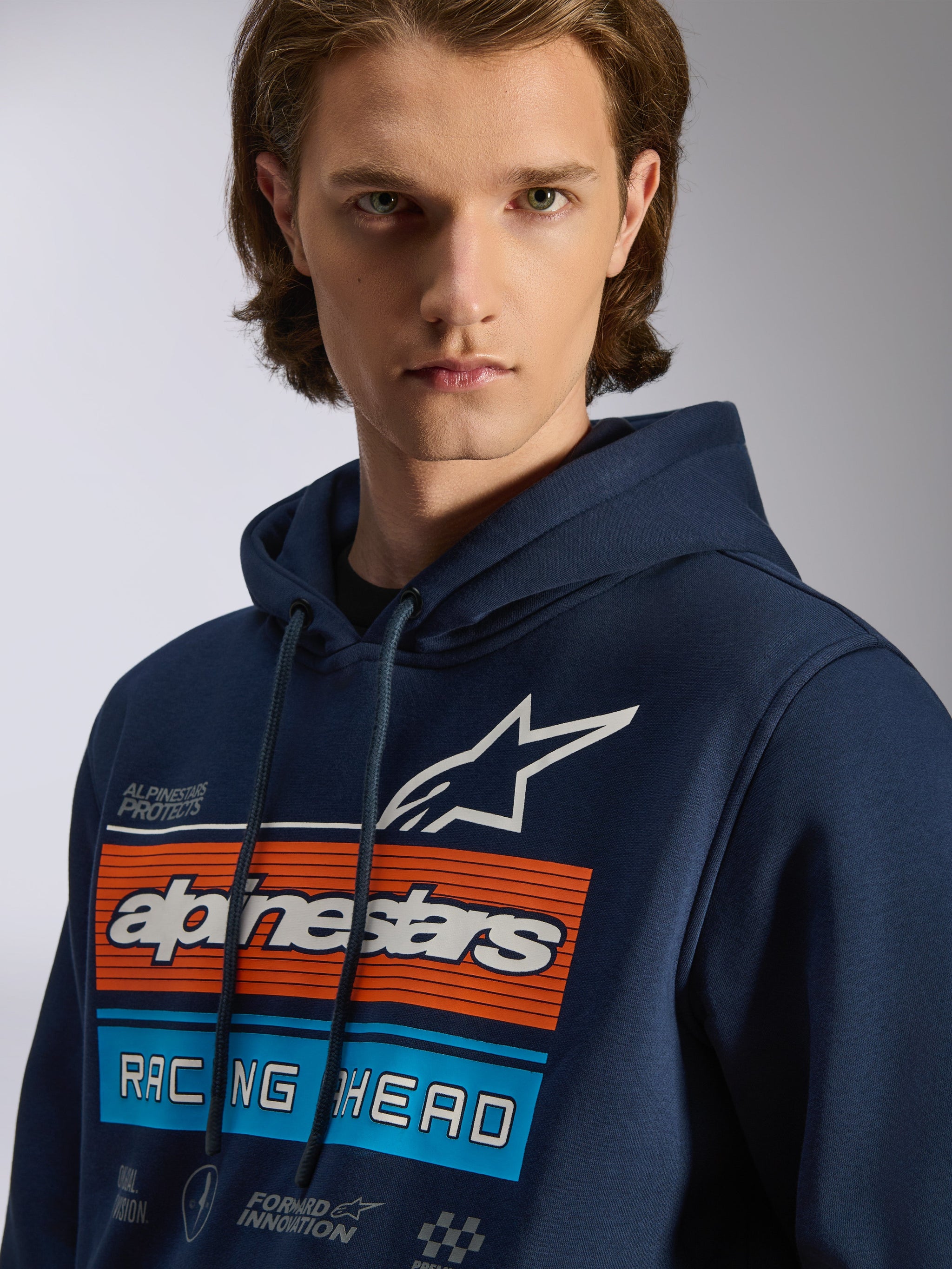 Sudadera con capucha Alpinestars Harken, sudadera azul marino para hombre, gráfico en el pecho con barras horizontales naranjas y azul claro, logotipo de estrella blanca y texto 'Racing Ahead', estilo urbano casual inspirado en el motorsport