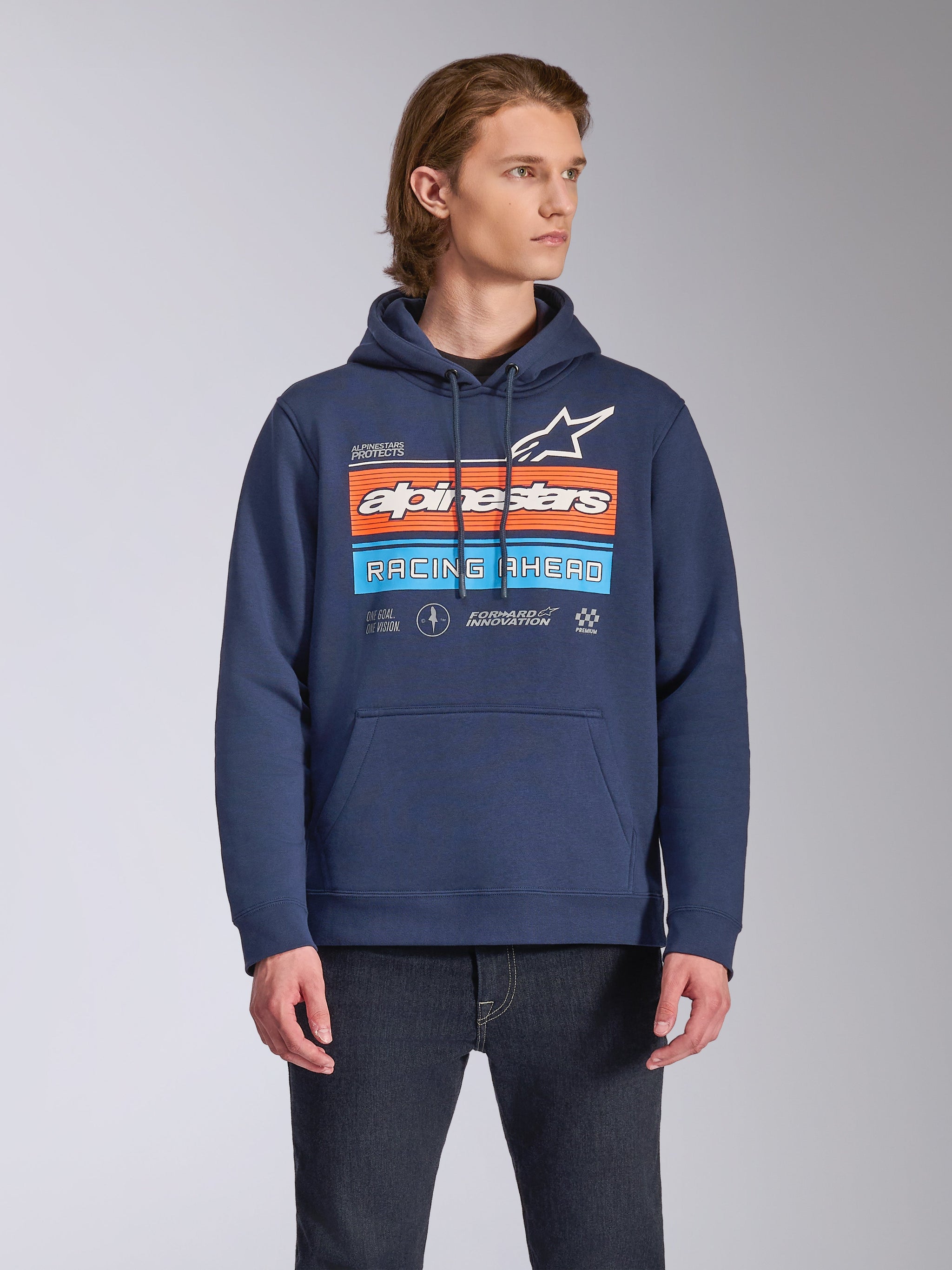 Alpinestars Harken Hoodie, ropa urbana casual, azul marino con gráfico 'Racing Ahead' en el pecho en naranja y azul claro, sudadera de forro polar con bolsillo canguro y capucha con cordón, lucida por un modelo con vaqueros oscuros