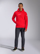 Modelo masculino luciendo la sudadera Alpinestars Frontal Hoodie en rojo, sudadera de forro polar con el logotipo Astars blanco en el pecho, bolsillo canguro y capucha con cordón, combinada con vaqueros gris oscuro y zapatillas altas negras, ropa urbana informal de estilo motorsport
