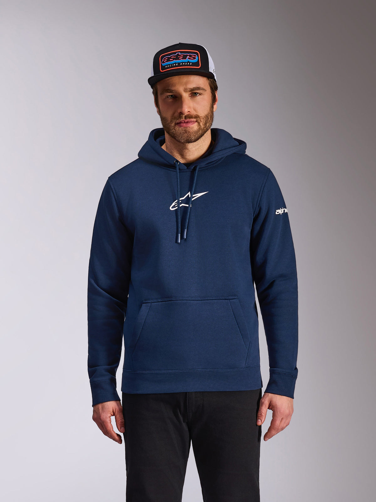 Sudadera con capucha Alpinestars Frontal, ropa casual de estilo motorsport, azul marino con el logo de Astars blanco en el pecho y logo de palabra blanco en la manga, bolsillo canguro, capucha con cordón, puesta por un modelo