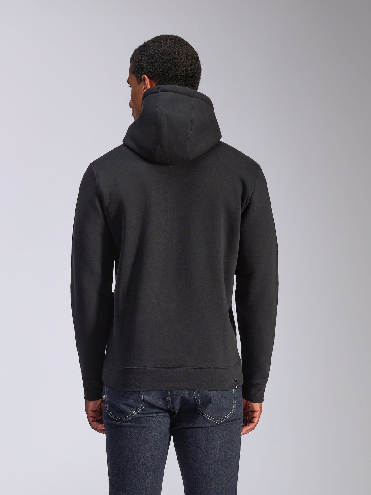Sudadera con capucha Alpinestars Blaze V3, vista posterior de sudadera negra de felpa, ropa de estilo urbano casual, con puños y dobladillo de canalé, capucha con forro de jersey, usada con vaqueros azul oscuro