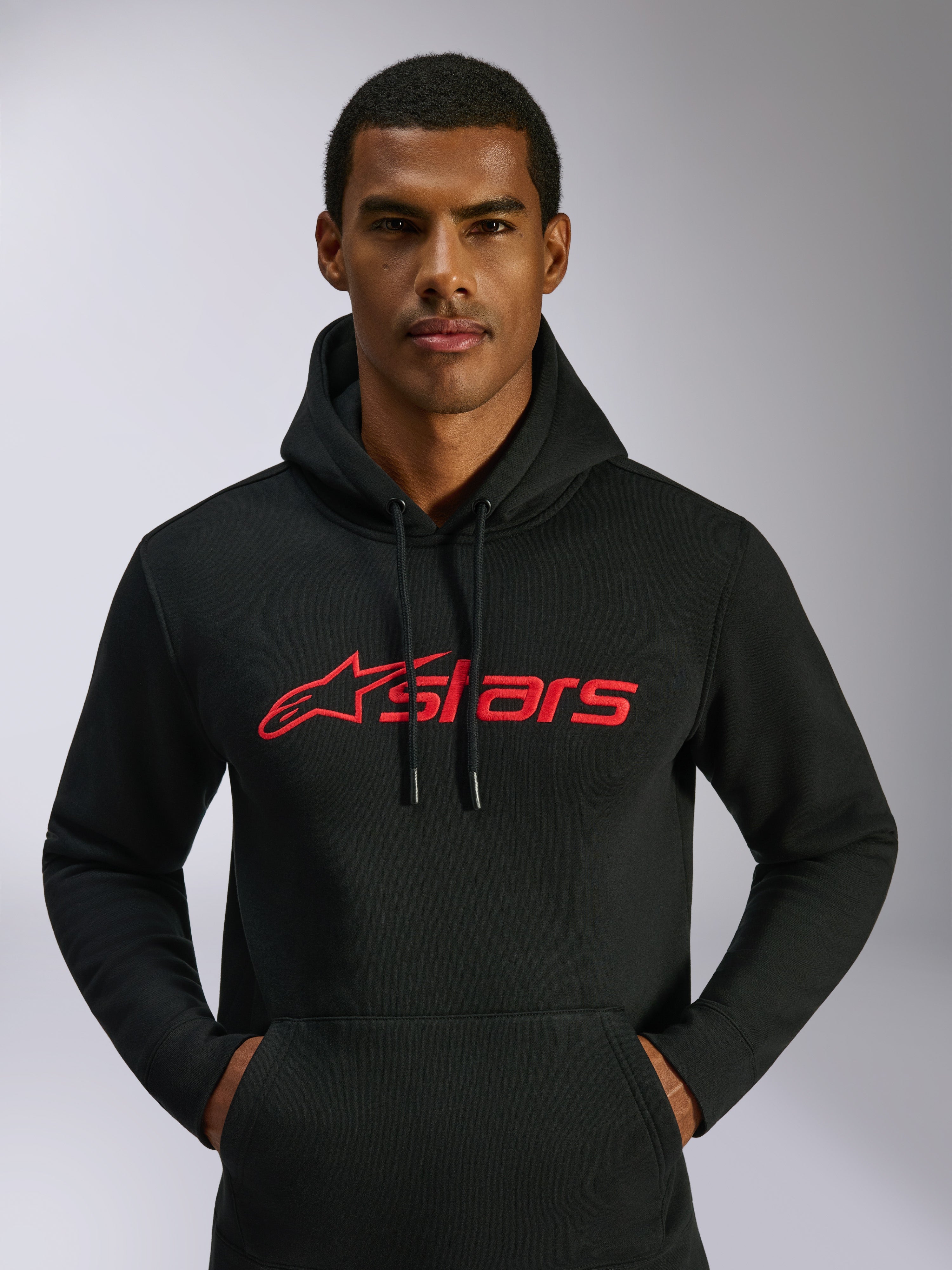 Sudadera con capucha Alpinestars Blaze V3, ropa urbana casual, negra con el logotipo de Alpinestars en rojo en el pecho, usada por un hombre, capucha con cordón, manga larga, diseño moderno inspirado en el motociclismo
