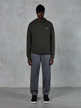 Model wearing Alpinestars Essentials Ageless Hoodie, casual streetwear, Off Black with small white logo on chest, paired with gray joggers, black beanie, and black sneakers, minimalist motorsport-inspired design