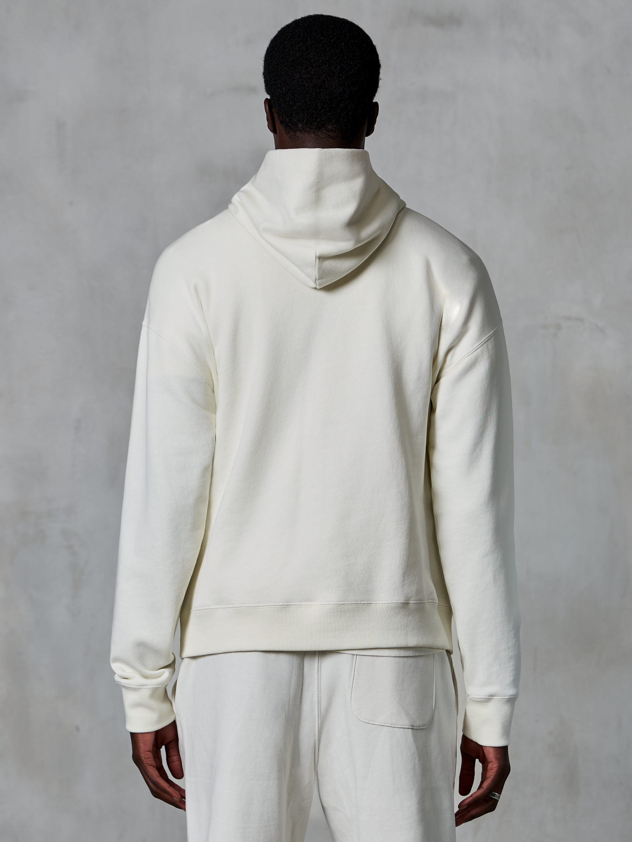 Alpinestars Essentials Ageless Hoodie, sudadera con capucha en color blanco roto, vista trasera en modelo, diseño minimalista y limpio, pantalones casuales a juego, ajuste relajado para comodidad diaria