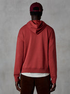 Alpinestars Essentials Ageless Hoodie, sudadera casual de forro polar, rojo ladrillo, vista trasera del modelo luciendo ropa lifestyle, con un diseño limpio con dobladillo y puños acanalados, combinada con pantalones de pana marrones y una gorra color burdeos