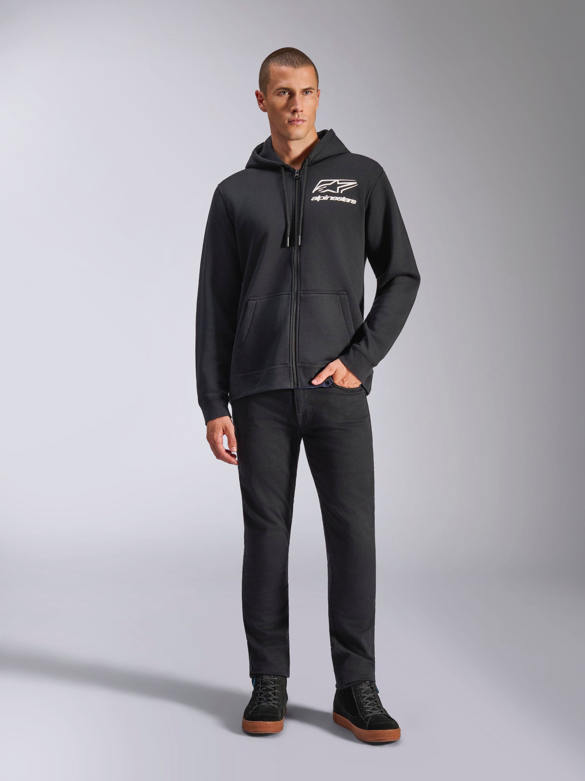 Alpinestars Formulation Hoodie, sudadera con capucha y cremallera completa, negra, logo blanco de Alpinestars en el pecho, combinada con pantalones negros y zapatillas, ropa casual de estilo de vida inspirada en el automovilismo