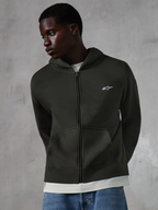 Sudadera con capucha y cremallera Alpinestars Essentials Ageless, estilo casual urbano en color Off Black, forro polar de cremallera completa con un pequeño logotipo blanco de Alpinestars en el pecho, mostrada por un modelo con vaqueros azules, con ajuste relajado, bolsillos delanteros y acabado lavado a la piedra.