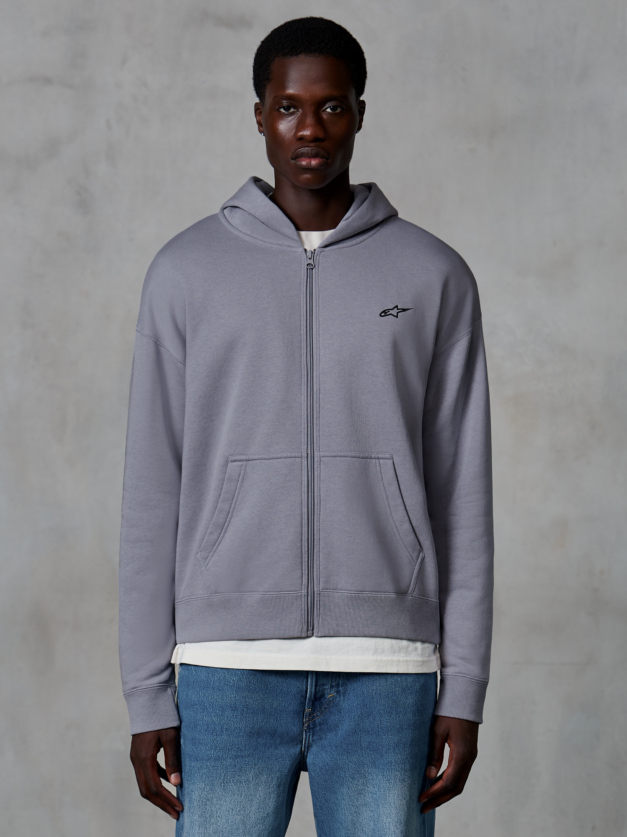 Alpinestars Essentials Ageless Zip Hoodie, color plata, ropa urbana casual usada por un modelo, sudadera de forro polar con cremallera completa, pequeño logo negro de Astars en el pecho, bolsillos de canguro, diseño de ajuste relajado