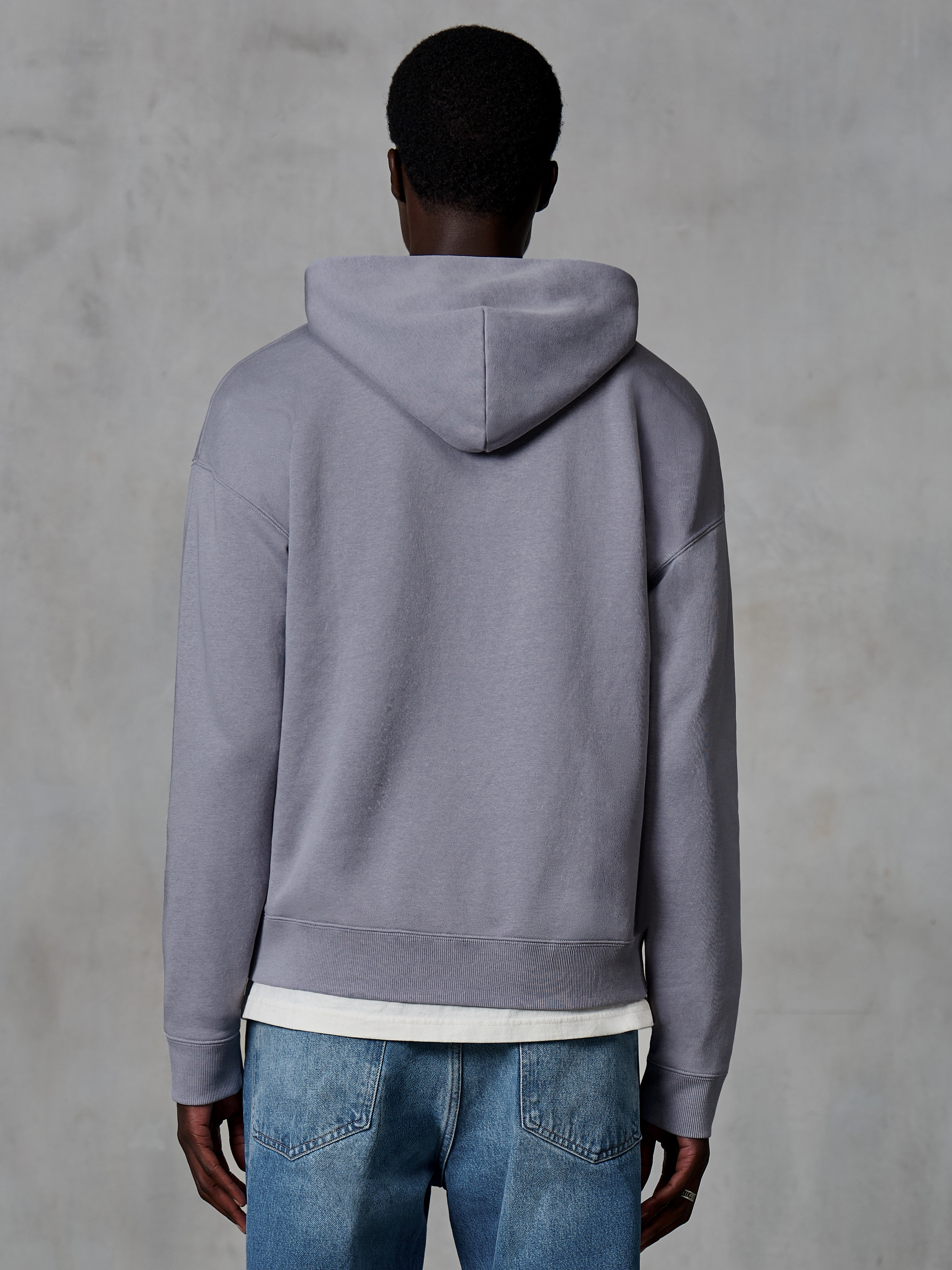 Sudadera con capucha y cremallera Alpinestars Essentials Ageless, plateada, vista trasera, estilo urbano casual, ajuste relajado con acabado de lavado a la piedra, combinada con vaqueros azules y camiseta blanca debajo