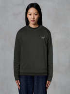 Alpinestars Essentials Ageless Crew, sudadera de cuello redondo premium, negro, con un pequeño logo blanco de Alpinestars en el pecho, estilo streetwear casual usada por una modelo con vaqueros oscuros