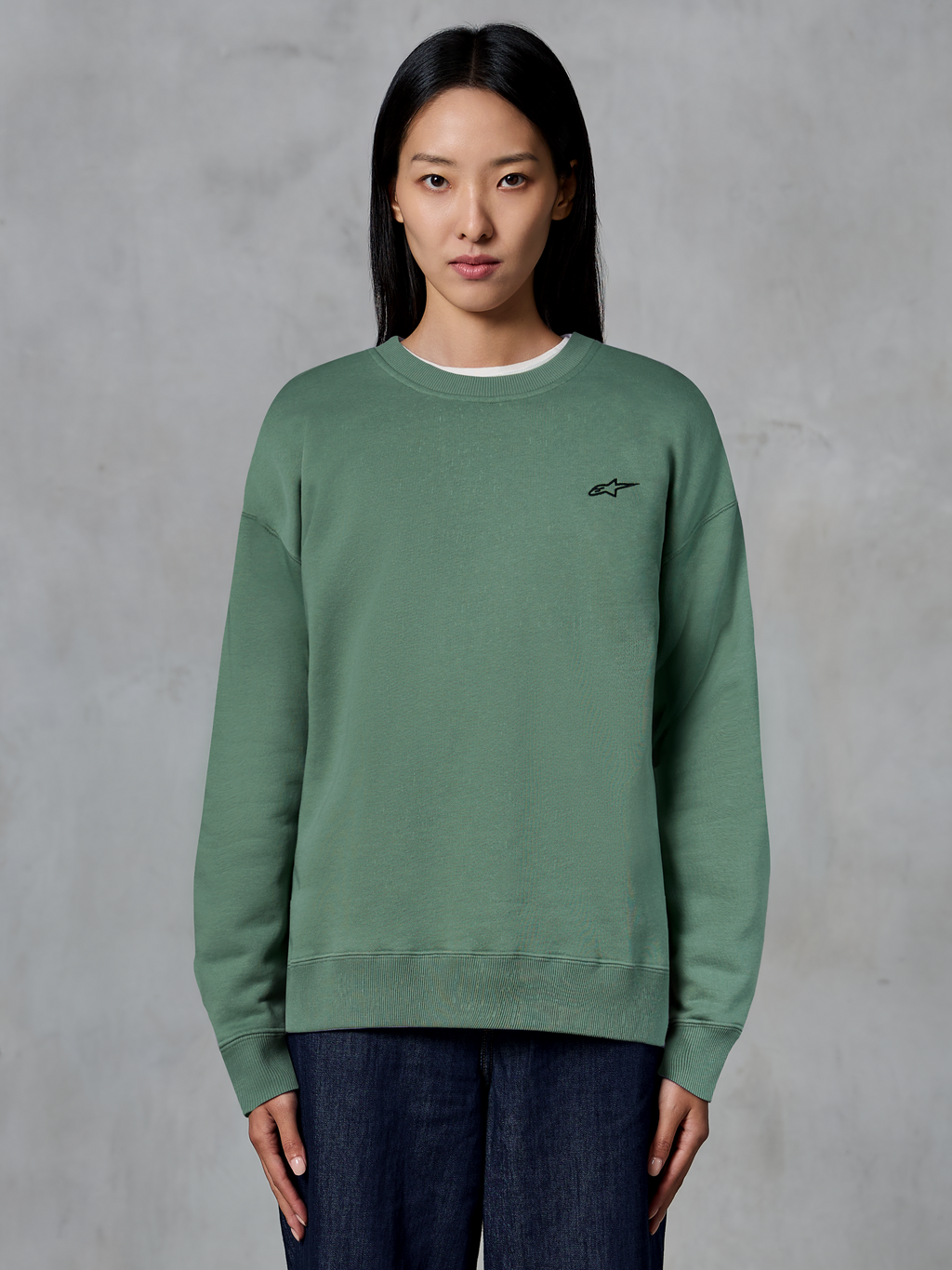Alpinestars Essentials Ageless Crew, sudadera de cuello redondo, verde cactus, lucida por una modelo, pequeño logotipo negro en el pecho, cuello, puños y dobladillo acanalados, ropa de calle casual de estilo motorsport