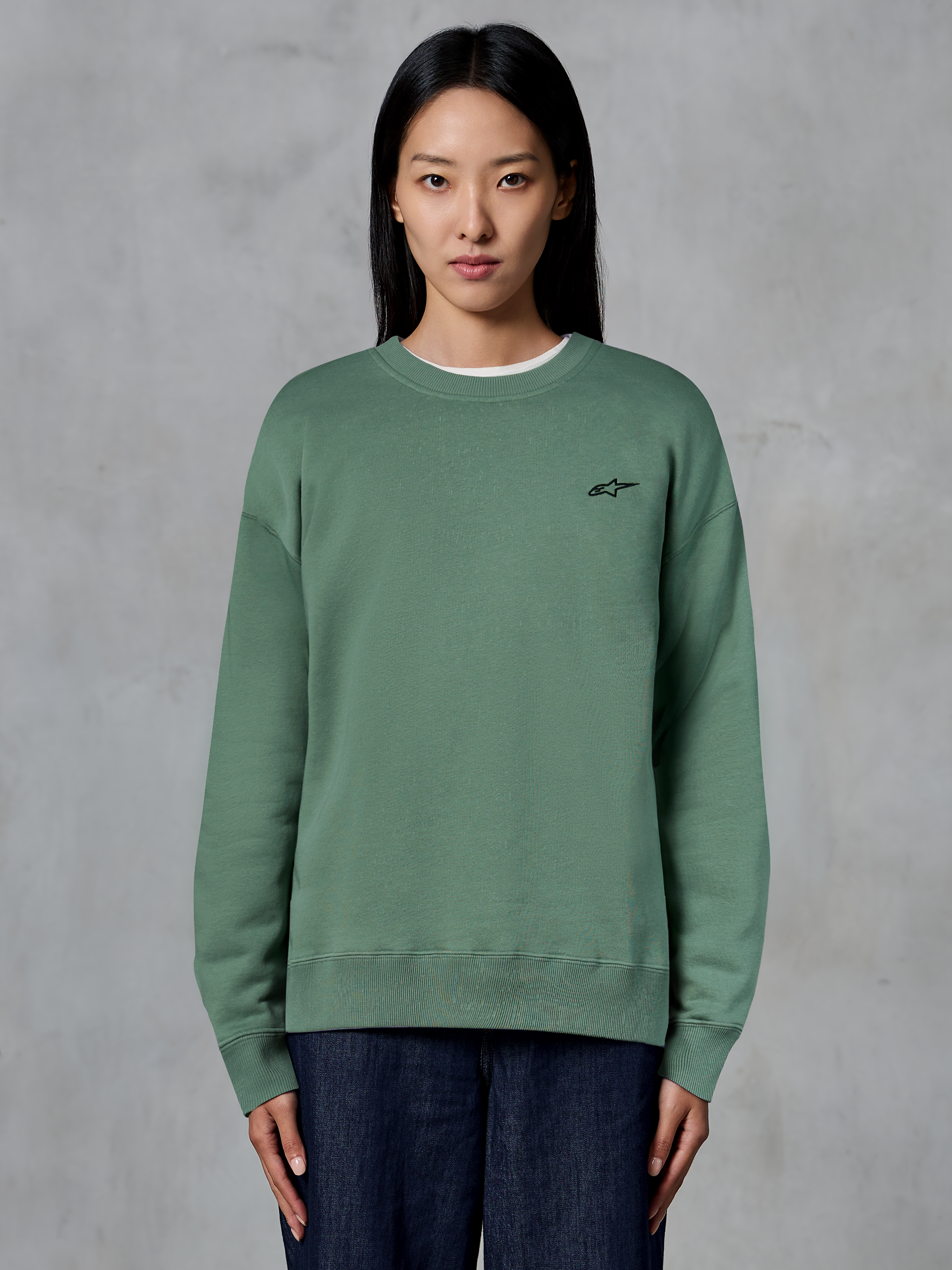 Alpinestars Essentials Ageless Crew, sudadera de cuello redondo, verde cactus, lucida por una modelo, pequeño logotipo negro en el pecho, cuello, puños y dobladillo acanalados, ropa de calle casual de estilo motorsport
