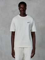 Camiseta Alpinestars Essentials Ageless SS, camiseta de manga corta, blanco roto, usada por un modelo masculino, con un pequeño logotipo negro de Alpinestars en el pecho, ajuste relajado, tejido de punto de algodón orgánico, estilo casual streetwear de motor