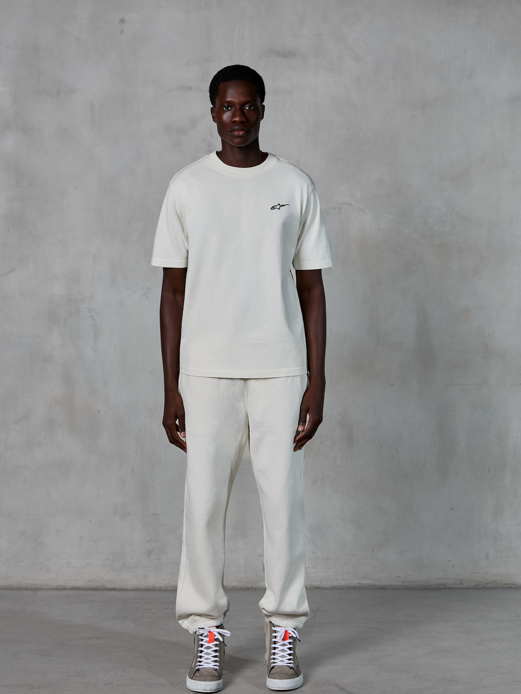 Alpinestars Essentials Ageless SS Tee, camiseta de manga corta, blanco roto, con un pequeño logotipo de Alpinestars en negro en el pecho, combinada con joggers a juego y zapatillas para un look de estilo de vida relajado