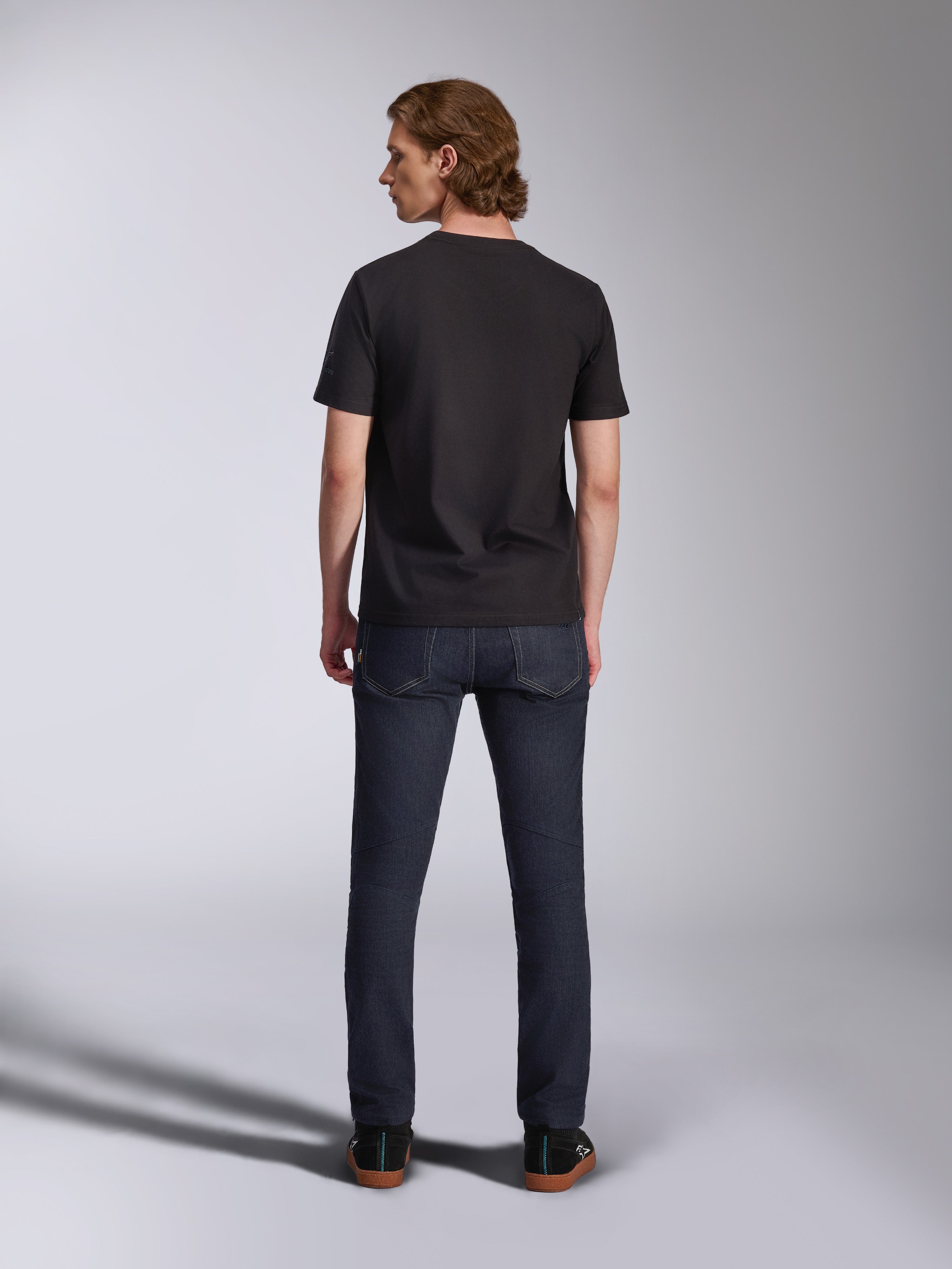 Alpinestars Global CSF Tee, Short Sleeve T-Shirt in Black, back view of male model wearing the shirt with dark denim jeans, casual motorsport-inspired streetwear