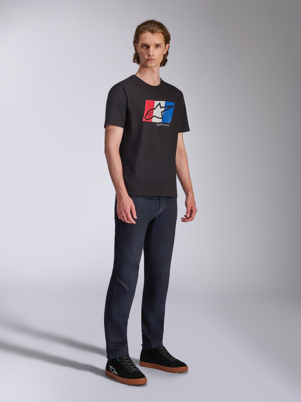 Alpinestars Global CSF Tee, Short Sleeve T-Shirt, Black with Red White and Blue Logo Graphic, Casual Motorsport Streetwear, Full body shot of model wearing dark jeans and black sneakers