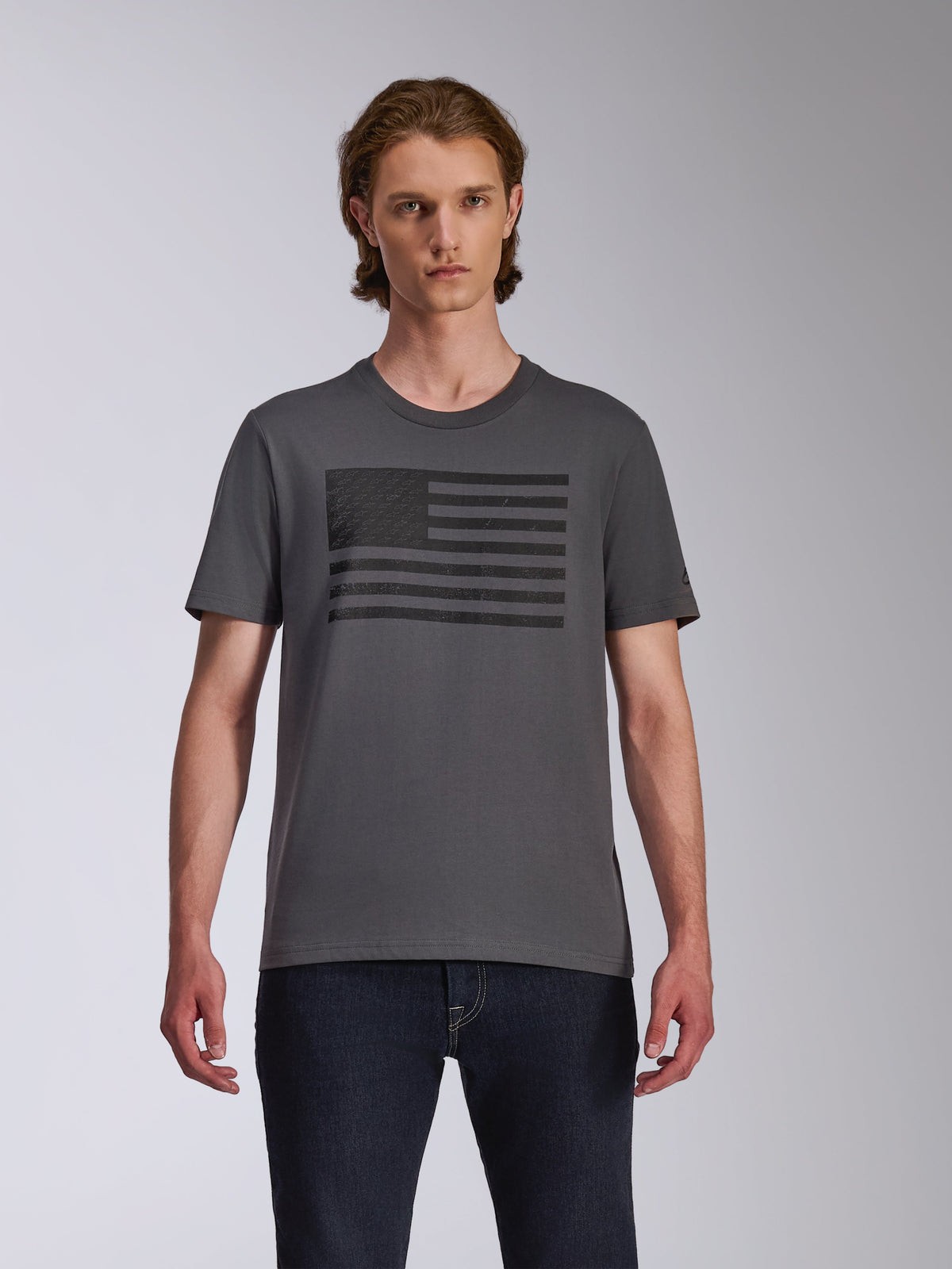 Alpinestars Waving CSF Tee, camiseta de manga corta, color carbón, con un gráfico del logotipo Blaze negro inspirado en una bandera en el pecho, usada por un modelo con vaqueros oscuros, estilo casual de motorsport streetwear
