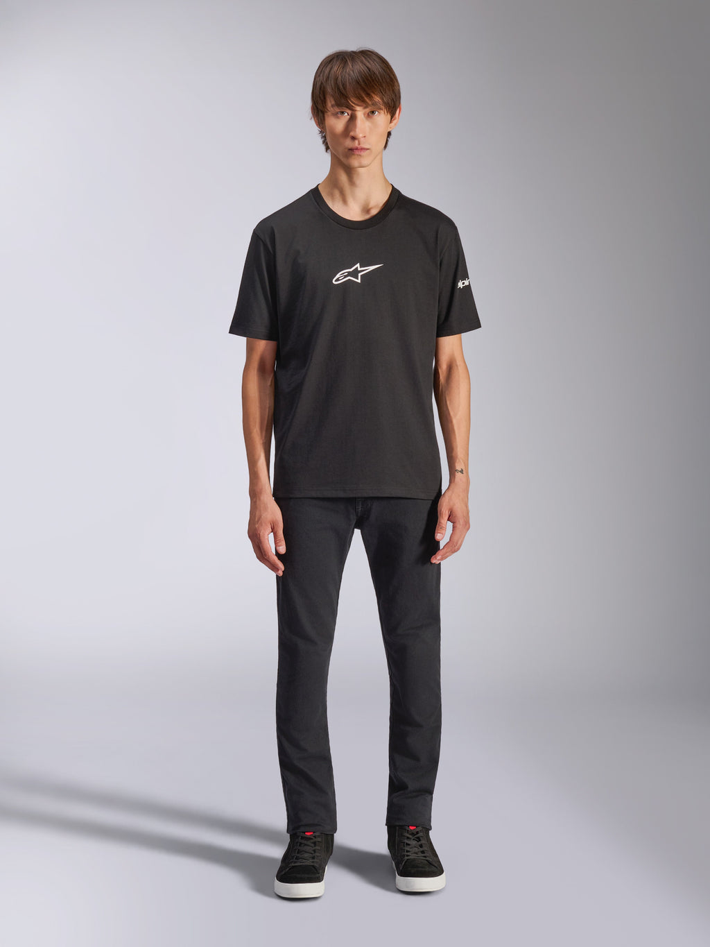 Alpinestars Frontal CSF Tee, camiseta de manga corta, negra, logotipo blanco de Alpinestars en el pecho, usada por un modelo con pantalones negros y zapatos negros, ropa deportiva casual de alto rendimiento