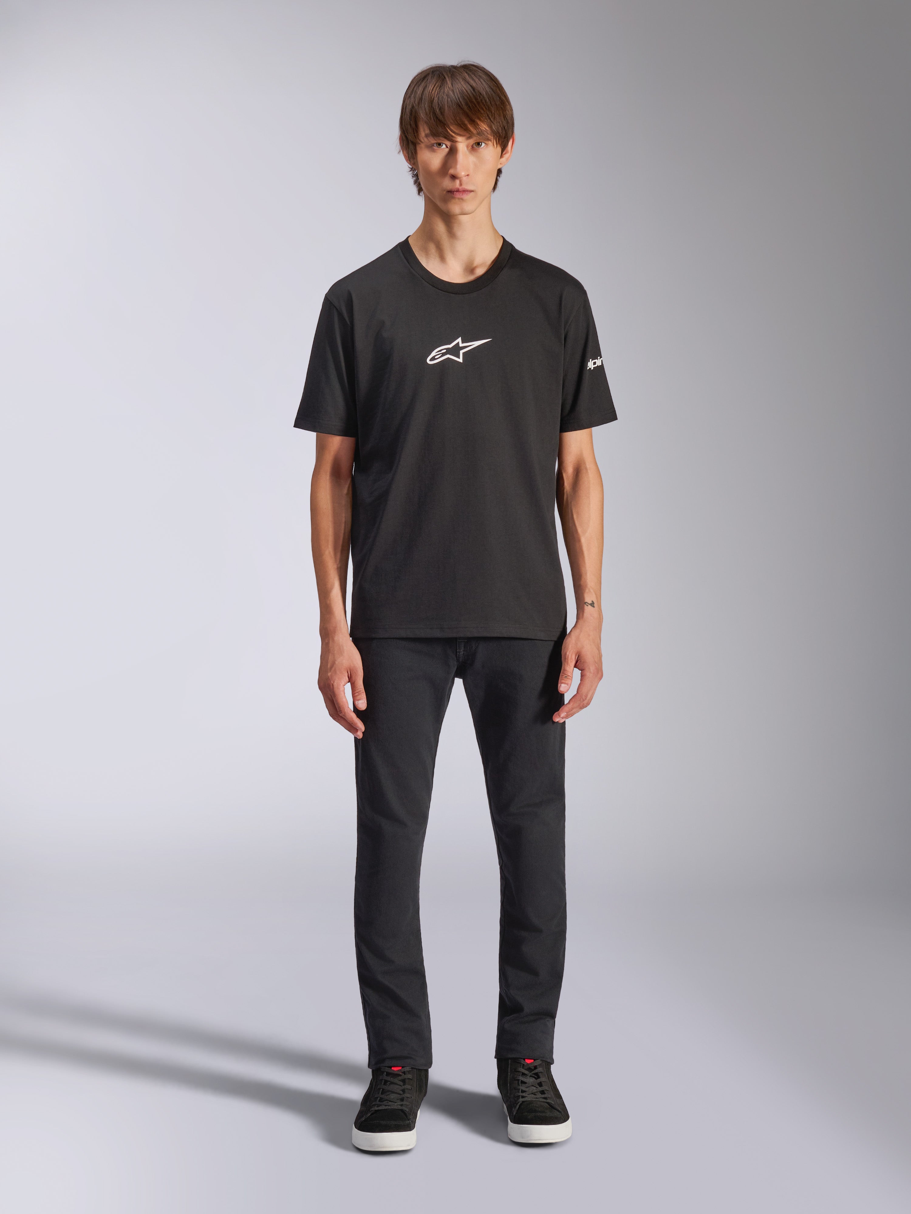 Alpinestars Frontal CSF Tee, camiseta de manga corta, negra, logotipo blanco de Alpinestars en el pecho, usada por un modelo con pantalones negros y zapatos negros, ropa deportiva casual de alto rendimiento