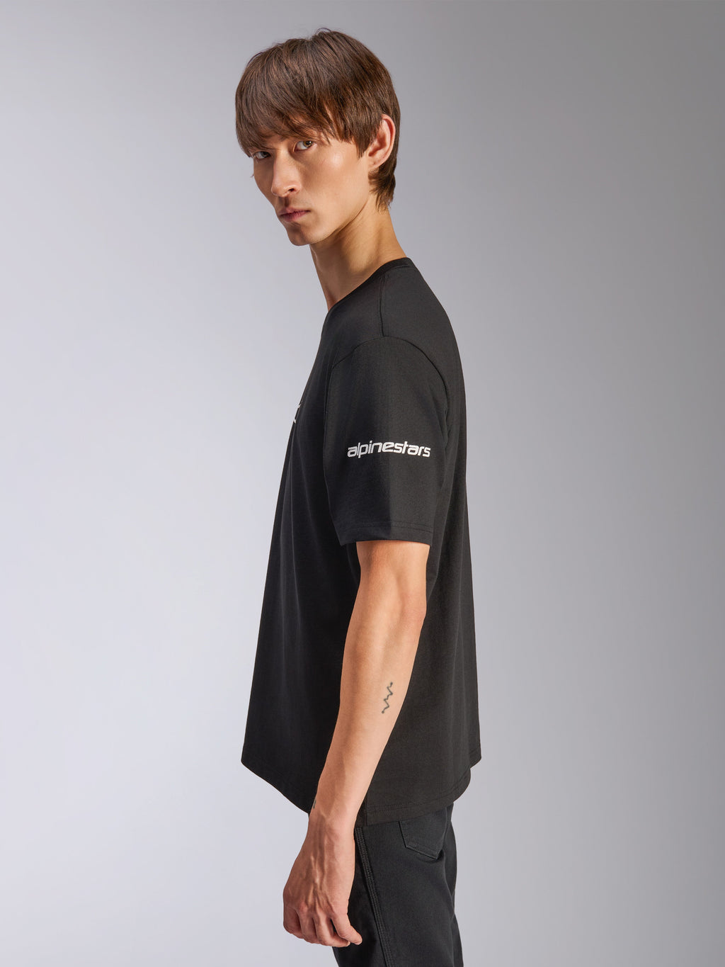 Camiseta Alpinestars Frontal CSF, camiseta de manga corta, negra, logotipo blanco de Alpinestars en la manga, usada por un modelo en vista de perfil, ropa urbana casual de alto rendimiento motorsport