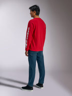 Alpinestars Trackside CSF Tee, camiseta de manga larga, roja, con el logotipo vertical de Alpinestars en blanco en la manga, lucida por un modelo con vaqueros azules y zapatillas negras, ropa urbana informal inspirada en el automovilismo