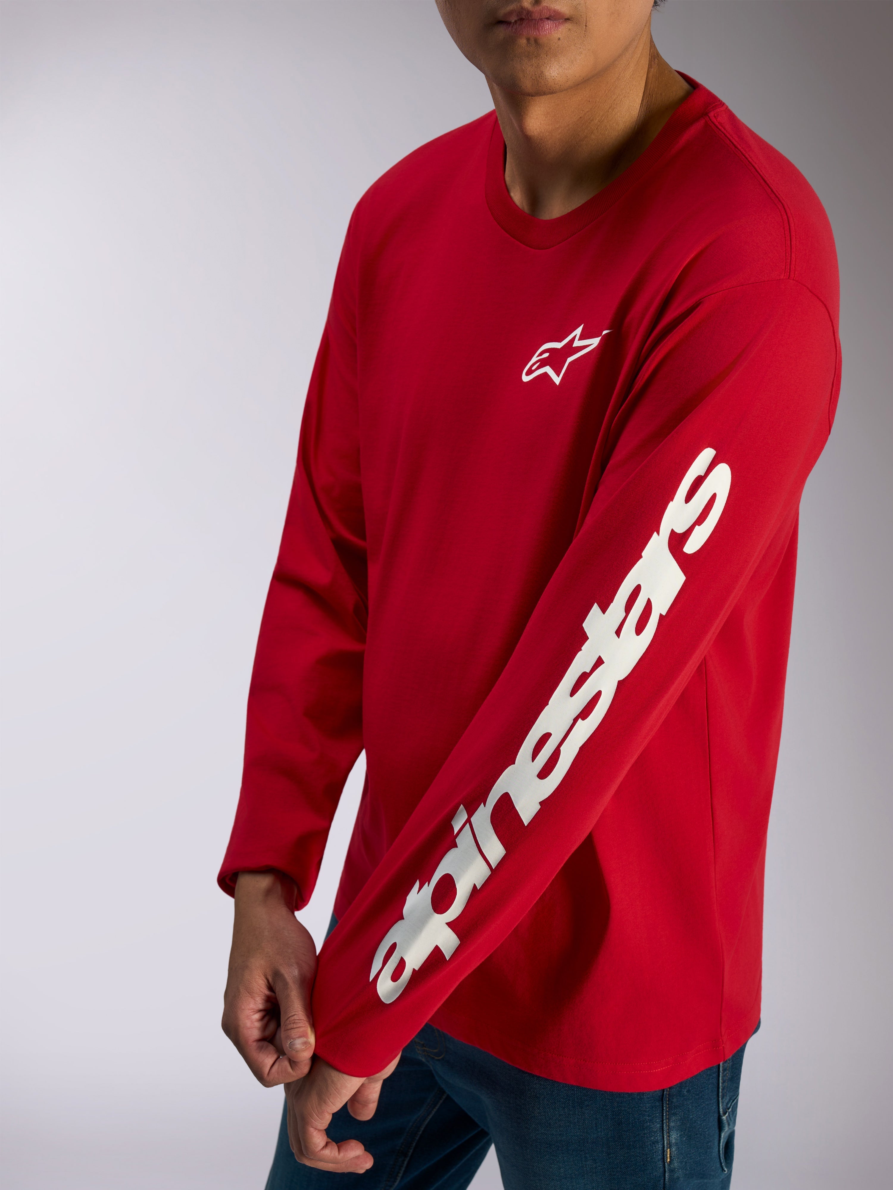 Alpinestars Trackside CSF Tee, camiseta de manga larga, roja, logotipo de Alpinestars en blanco en el pecho y marca denominativa llamativa en la manga, estilo streetwear casual de automovilismo usada con vaqueros azules
